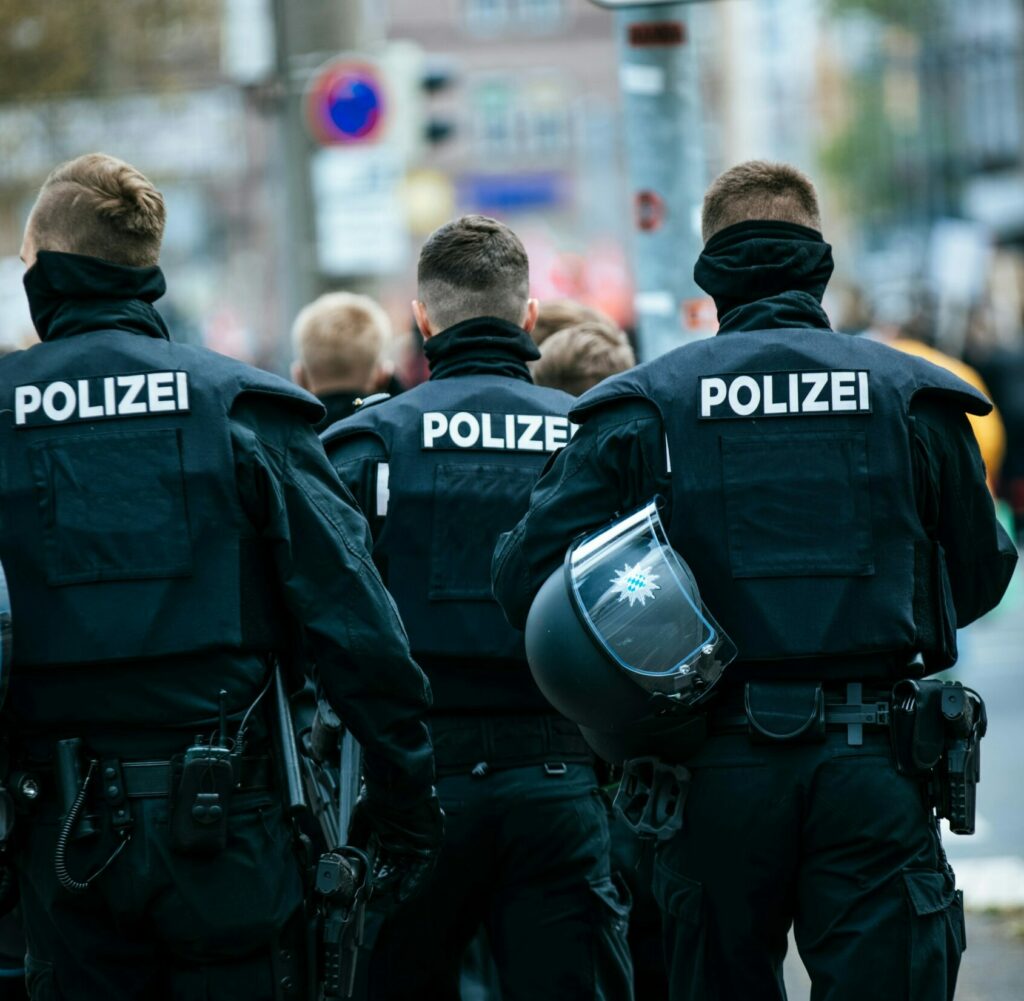 Das Beitragsbild ist auch das Bild, das wir für unseren Post "Extremismus bei der Polizei?" genutzt haben. Es zeigt drei Bereitschatspolizisten, die mit dem Rücken zur Kamera an einer Straße stehen.